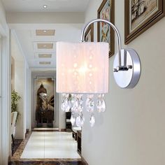 a white lamp hanging from the side of a wall next to a hallway with pictures on the walls