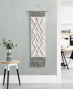 a white wall hanging next to a table with a potted plant on top of it