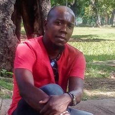 a man is sitting on the ground in front of some trees and has his arms crossed