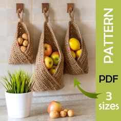 three bags hanging on the wall with apples and potatoes in them next to a potted plant