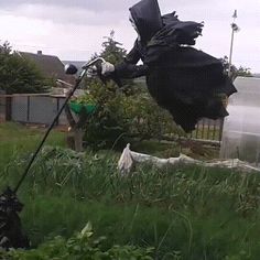 a scarecrow is in the yard with his arms out to grab something from a trash can