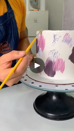 a person is decorating a cake with purple flowers