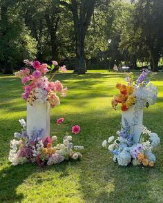 two white vases filled with colorful flowers sitting on top of a lush green field