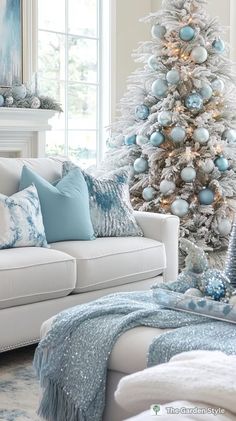 a living room decorated for christmas with blue and silver ornaments on the tree, white couches and fireplace