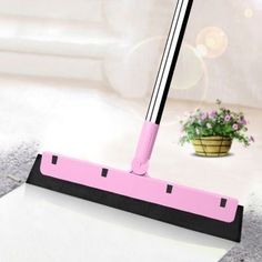 a pink dust mop sitting on top of a white floor next to a potted plant