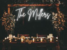 a table topped with candles and flowers next to a neon sign that says the millers