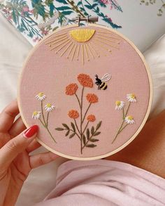 a woman is holding up a pink embroidery hoop with flowers and a bee on it