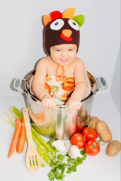 a baby sitting in a pot with vegetables around it