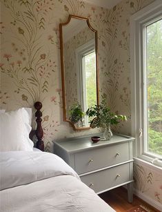 a white bed sitting under a large mirror next to a dresser with flowers on it