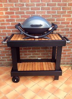 an outdoor bbq grill on wheels with a brick wall in the background