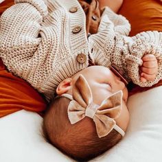 a baby laying on its back wearing a sweater and a bow tie around it's head