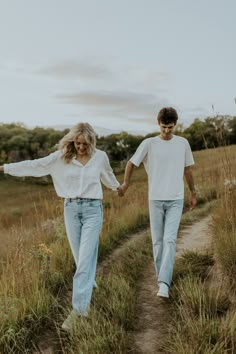 a man and woman walking down a path holding hands in the middle of a field