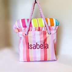 a pink and white striped tote bag with personalized name on the front hanging from a hook