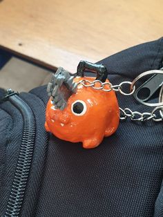 an orange plastic animal keychain on top of a piece of luggage with chains