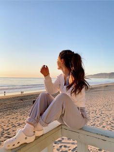 a woman sitting on top of a wooden bench next to the ocean at sunset or sunrise