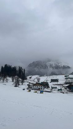 a snowy landscape with houses and trees in the background, on a cloudy day near some mountains