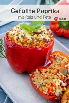 stuffed bell peppers with rice and vegetables on a white platter next to some tomatoes