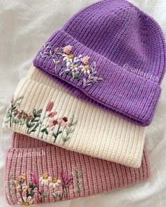 three knitted beanies with flowers on them sitting on top of a white sheet