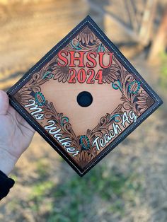 a person holding up a graduation cap with the words hsu 202 on it in front of a field