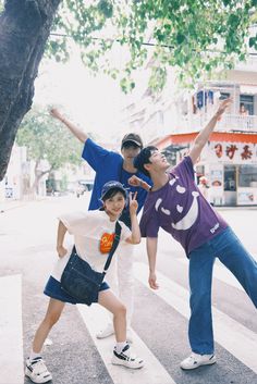 three boys are standing in the street and one boy is holding his arms up to the sky