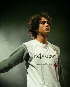 a man with curly hair wearing a white shirt and holding his arms out to the side