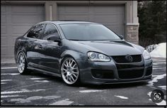 a gray car parked in front of two garage doors with snow on the ground behind it