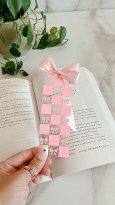 a person is holding an open book with pink and silver squares on it, next to a plant