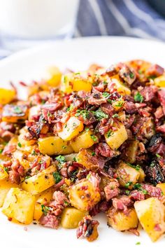 a white plate topped with potatoes covered in bacon and parsley next to a glass of milk