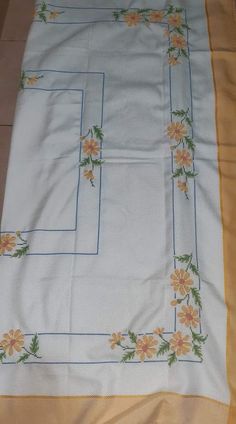 a white table cloth with yellow and orange flowers on the border is laying on a tile floor