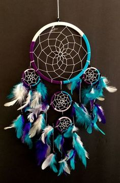 a blue and purple dream catcher hanging from a hook on a black wall with feathers