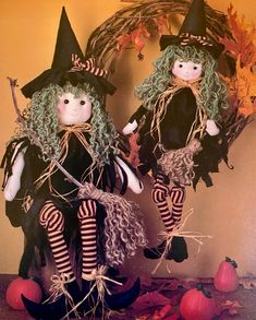 two dolls dressed in black and green sitting next to each other with pumpkins on the ground