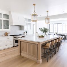 a large kitchen with white cabinets and wooden flooring is pictured in this image, there are many chairs around the island