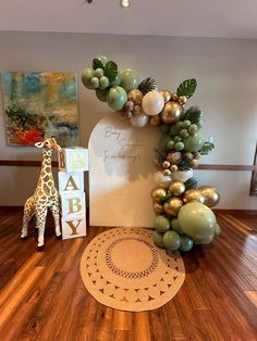 a giraffe is standing next to a baby's first birthday sign and balloon garland