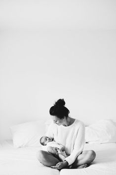 a woman sitting on top of a bed holding a baby