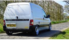 a white van parked on the side of a road next to some grass and trees