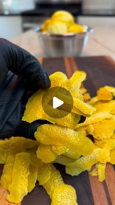 a person in black gloves is peeling yellow peels on a cutting board with a bowl of oranges behind them