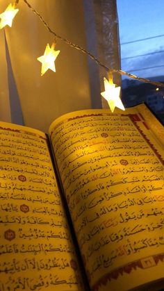 an open book with arabic writing on it and lights strung from the pages in the background