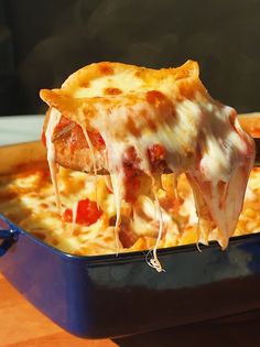 a slice of pizza being lifted from a blue casserole dish on a wooden table