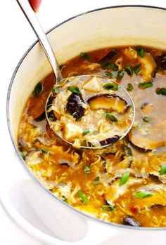 a ladle full of soup with mushrooms and greens