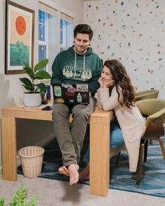 a man and woman sitting at a desk in an office with plants on the wall