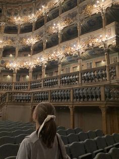 a woman standing in front of an auditorium filled with chairs and chandelier lights