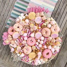 a plate filled with lots of pink donuts on top of a wooden table next to a striped napkin