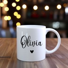 a white coffee mug sitting on top of a wooden table with lights in the background