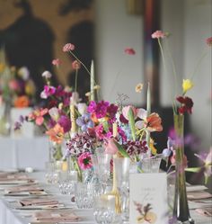 there are many vases with flowers in them on the long table, along with place cards