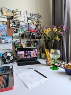 a laptop computer sitting on top of a white desk next to a vase with flowers