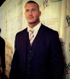 a man wearing a suit and tie standing in front of a wall with writing on it