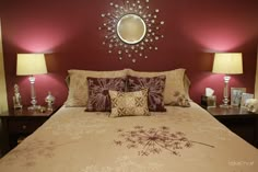 a large bed with pillows and lamps on either side of the headboard, in front of a red wall