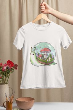 "Step into a magical realm with our Enchanted Forest Snail T-Shirt! This whimsical unisex tee captures the imagination with a charming snail whose shell blossoms into a miniature ecosystem of vivid mushrooms and sparkling crystals. Each shirt is printed on high-quality, soft cotton for a comfortable fit and designed to appeal to nature lovers of all ages. Available in a variety of sizes, this graphic tee makes for a perfect gift or a delightful addition to your own wardrobe. Experience the fusion of comfort and fantasy with our uniquely designed T-shirt that promises to stand out in any setting. Add a touch of enchantment to your everyday style! We utilize the authentic Bella Canvas 3001 brand, renowned for its UNISEX design, making it one of the most sought-after shirts in the market. Pri Mushroom Crystal, Family Vacation Shirts, Crystal Design, Vacation Shirts, Gifts For Nature Lovers, Enchanted Forest, Nature Lovers, Family Shirts, Everyday Style