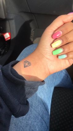 a woman's hand with colorful nails and a triangle tattoo on her left wrist