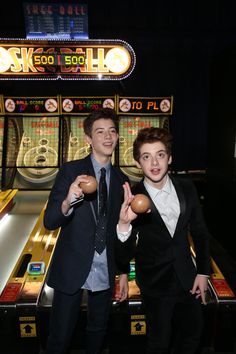 two young men standing next to each other in front of a pinball game machine